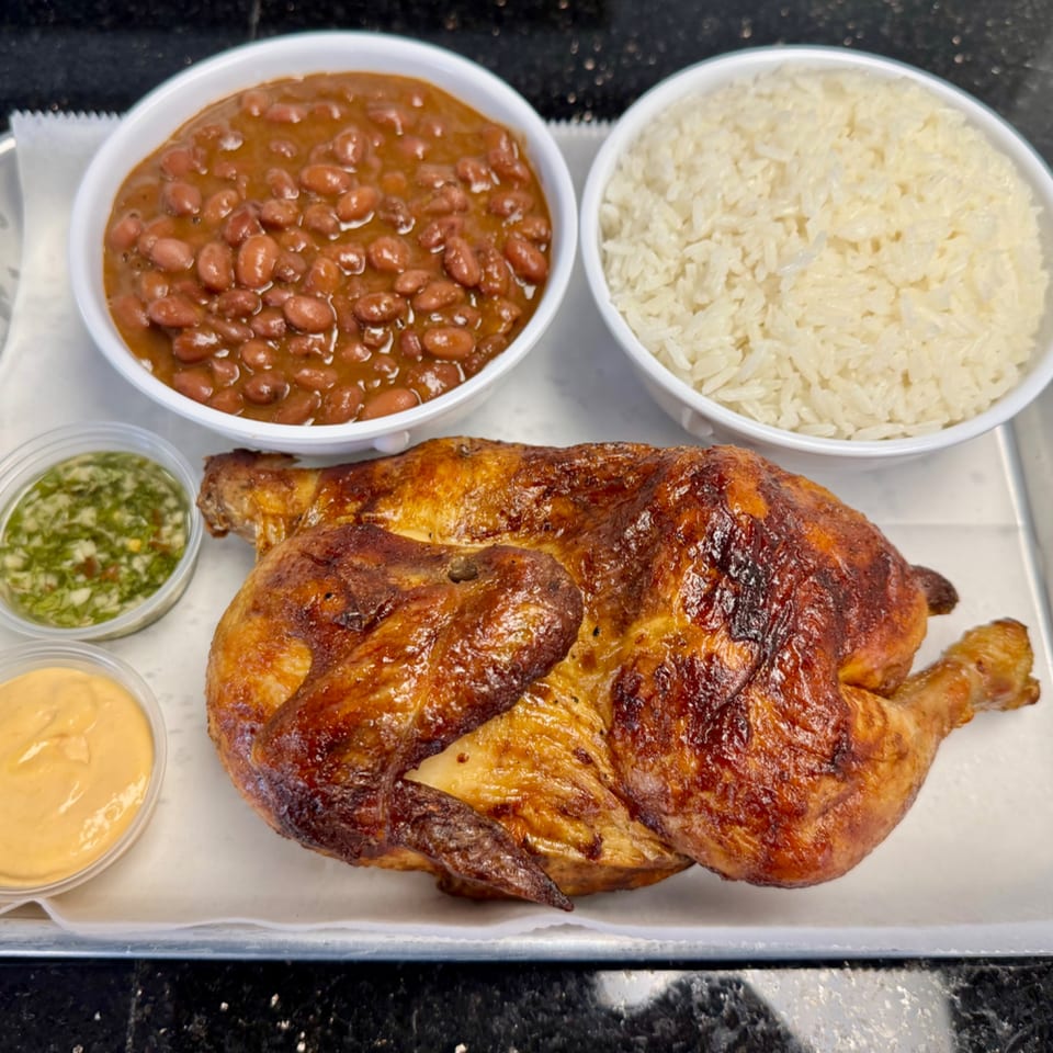A whole roasted chicken with sides of rice, beans, and two dipping sauces on a tray.
