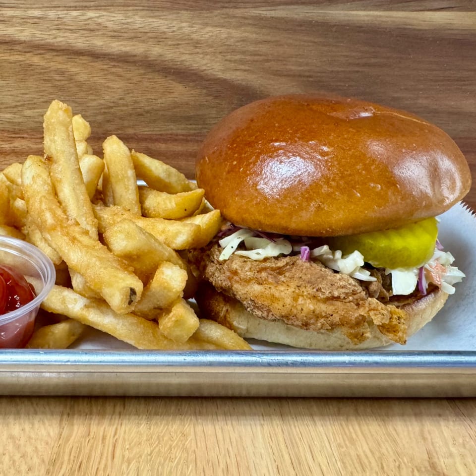 Crispy fried chicken sandwich with coleslaw and pickles, served with golden fries and ketchup.