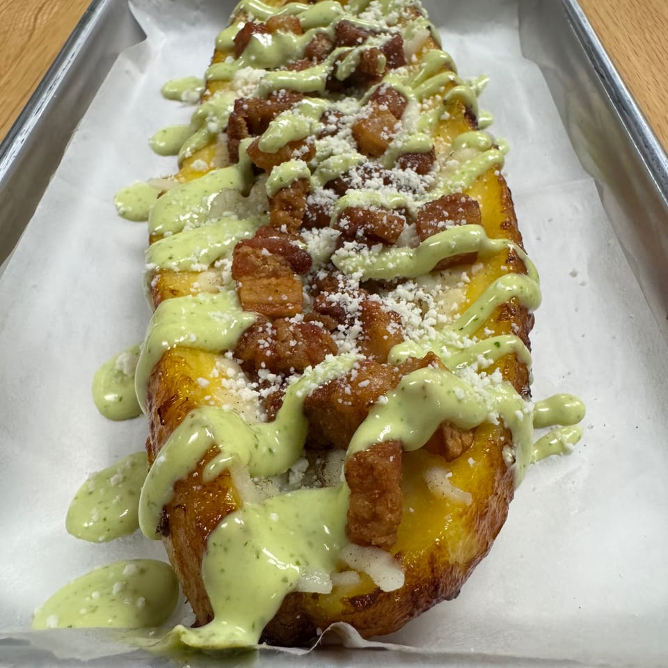 Golden fried plantain topped with crispy chicken, green sauce, and white cheese crumbles.