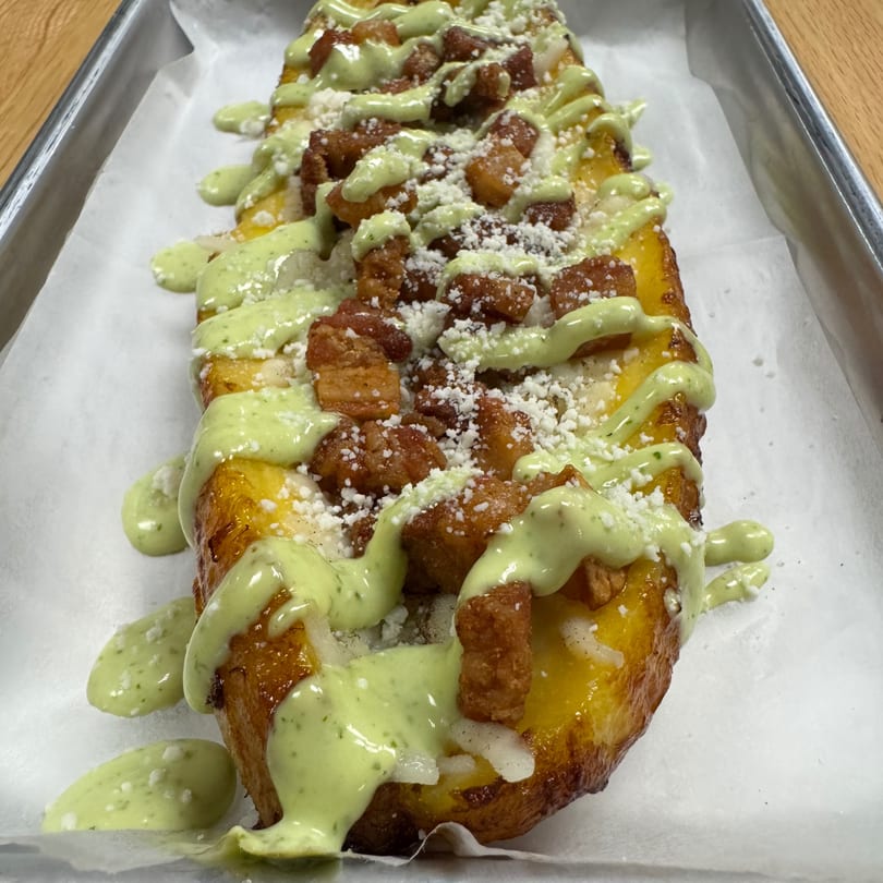 Golden fried plantain topped with crispy chicken, green sauce, and white cheese crumbles.