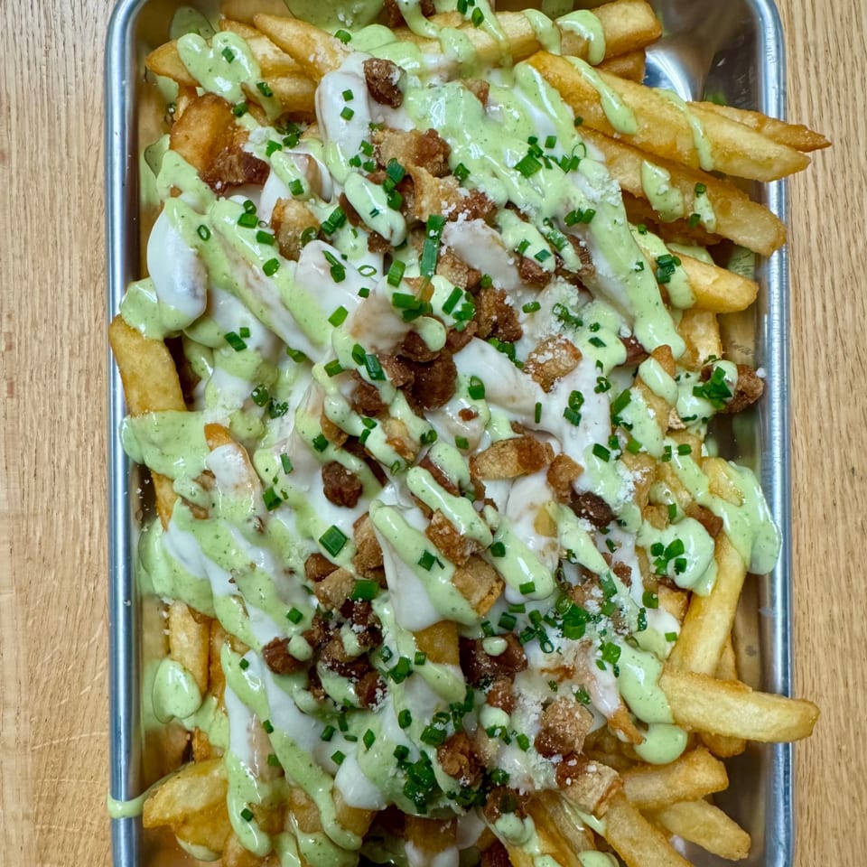 Chicken Supreme's loaded fries with green and white sauces, crispy chicken, and chives in a metal tray.