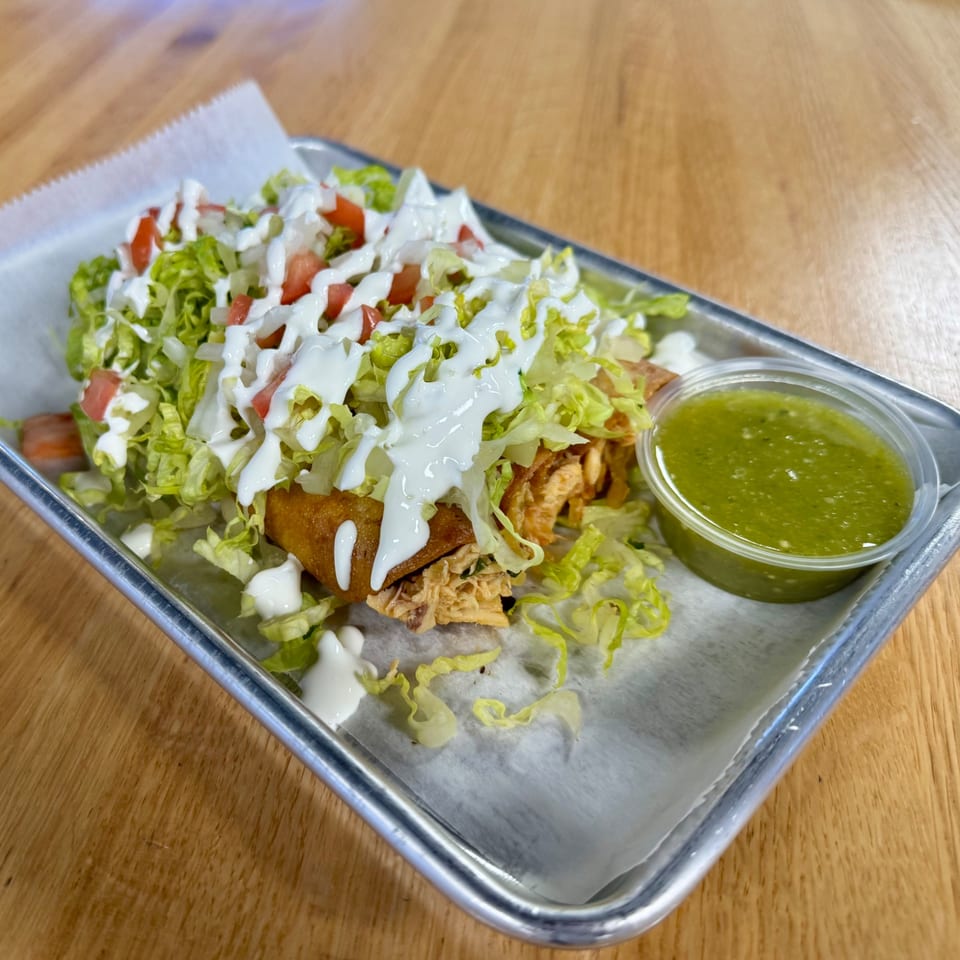 Chicken Supreme's fried chicken taquitos topped with lettuce, tomato, sour cream, and a side of green salsa.