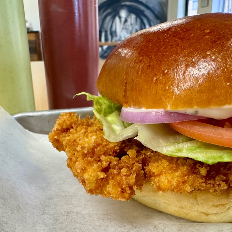 A crispy fried chicken sandwich with lettuce, tomato, onion, and mayonnaise on a brioche bun.